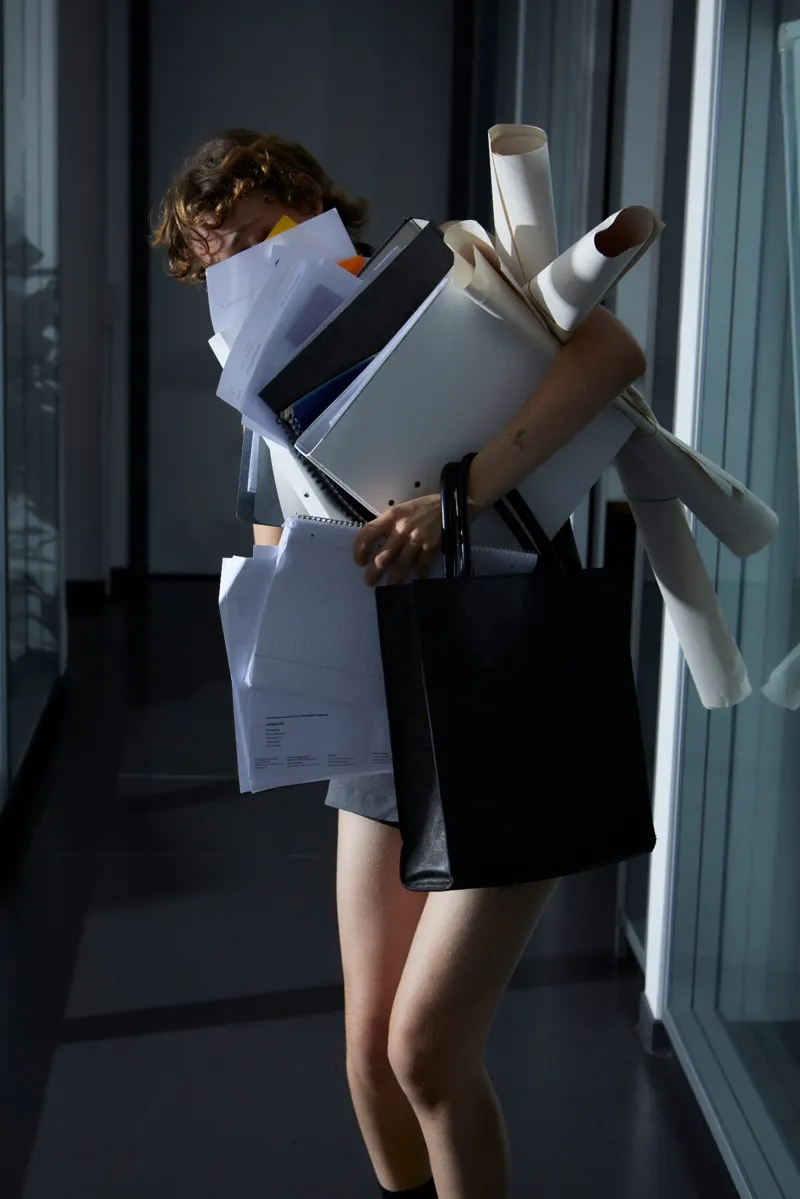 A woman carrying an armful of rolled paper — more than two arms should hold.