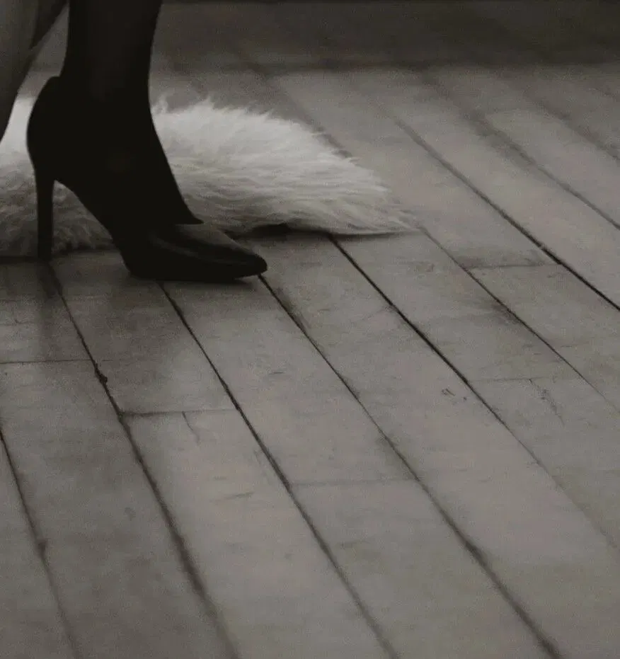 Close crop of a black heel on bare floorboards beside a pale fur.