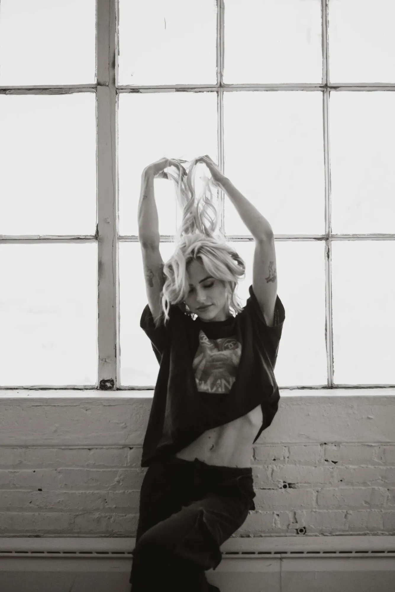 Figure standing inside a large industrial steel window grid, arms raised overhead.