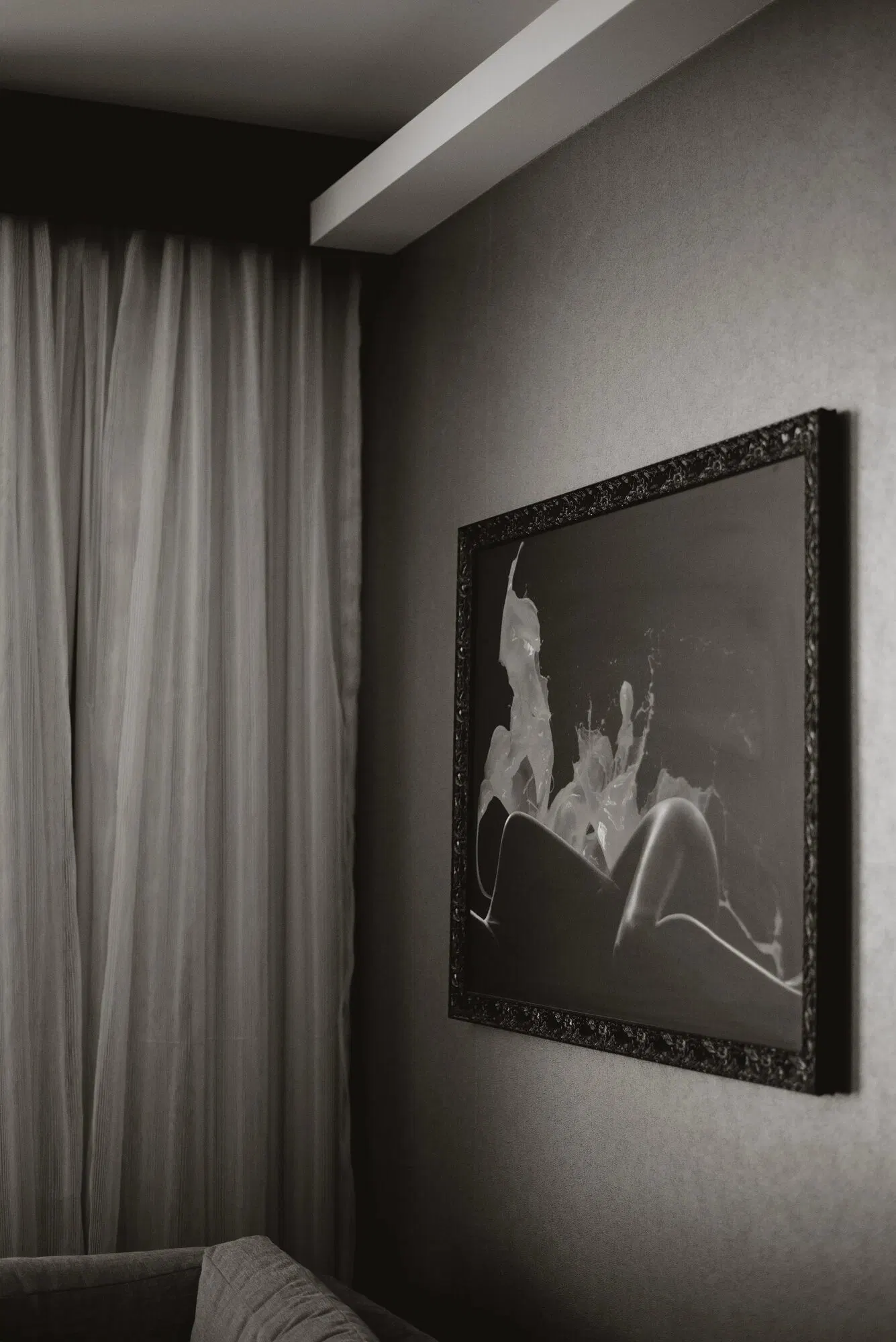 A large framed photographic print on the wall of a low-lit hotel room, curtain edge in frame.