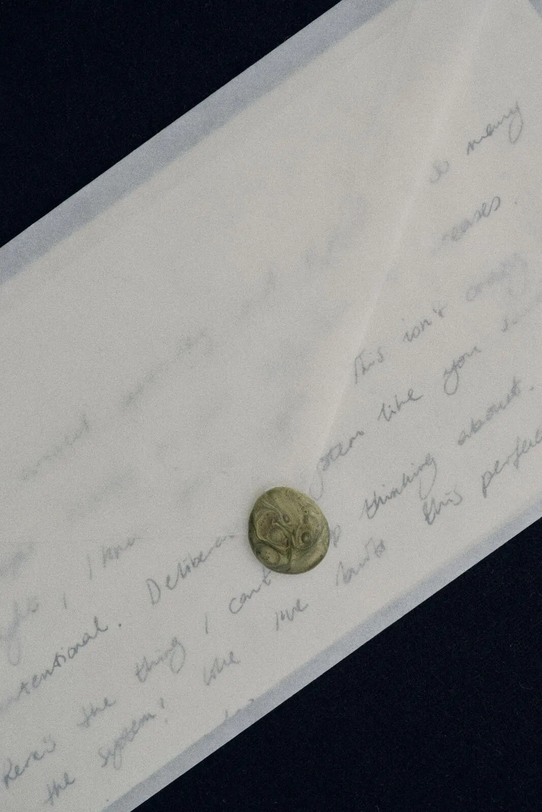 A handwritten letter under vellum, closed with a pale wax seal, on a near-black surface.