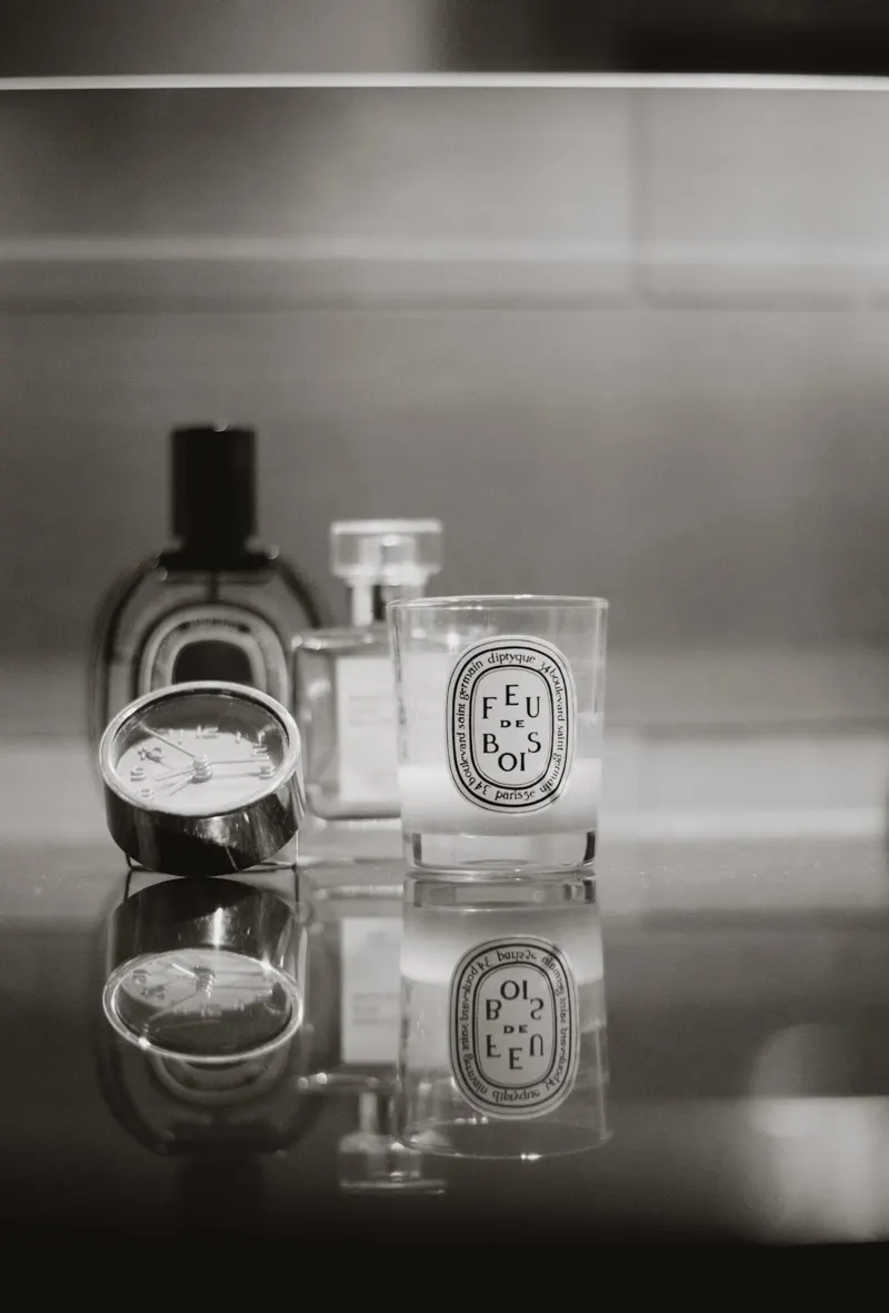 Glass candle vessels and perfume on a reflective marble surface, still life.