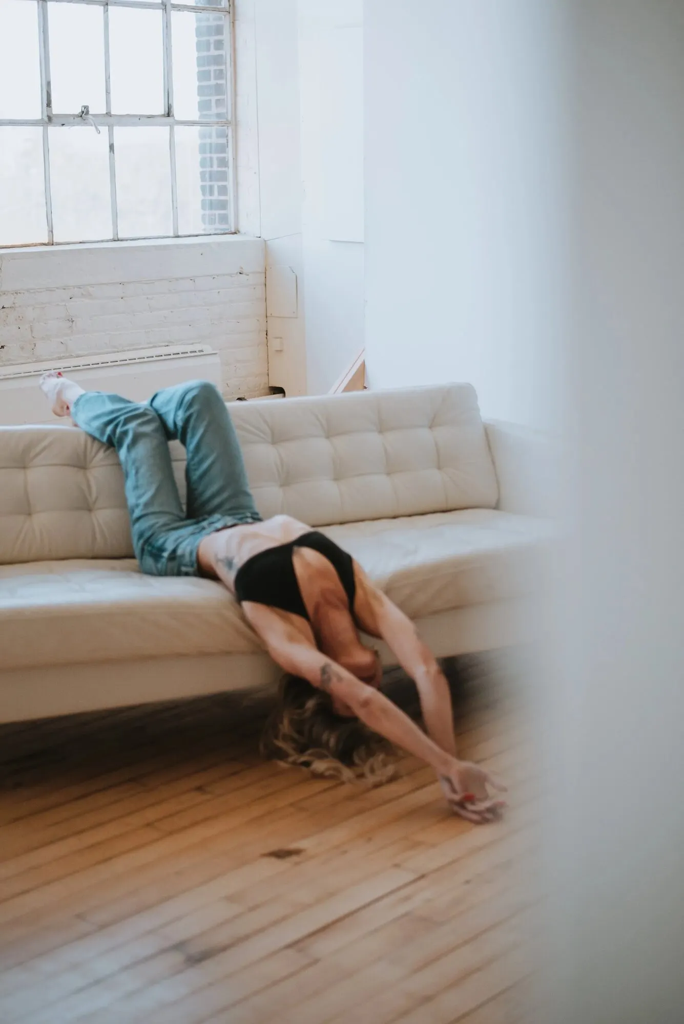 Figure reclining across a cream sofa in a bright room with tall windows.